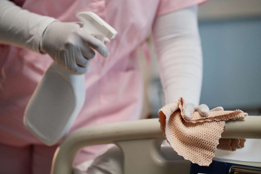 Cleaner wiping the side of bed frames in Hospital